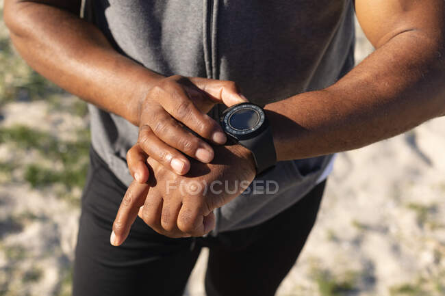 Mittlerer Abschnitt des fitten afrikanisch-amerikanischen Mannes beim Trainieren der Smartwatch. gesunde Ruhestand Technologie Kommunikation Outdoor Fitness Lebensstil. — Stockfoto