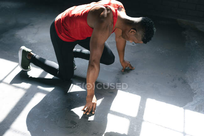 Африканський американець у спортивному одязі на колінах починає працювати у порожньому міському будинку. Здоровий спосіб життя в місті. — стокове фото