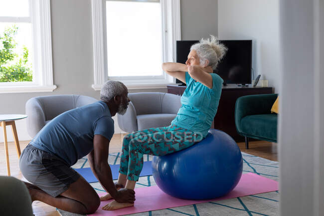 Старшая пара смешанных рас в спортивной одежде, тренирующаяся в гостиной. оставаться дома в изоляции во время карантинной изоляции. — стоковое фото