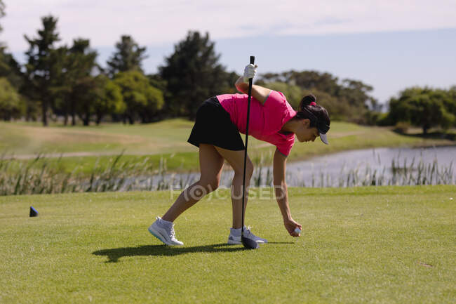 Mujer caucásica jugando al golf inclinada a colocar la pelota antes de disparar. deporte ocio aficiones golf estilo de vida al aire libre saludable. - foto de stock