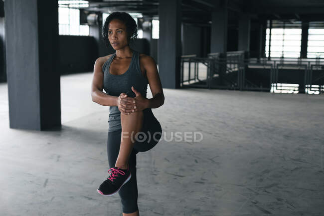 Femme afro-américaine debout dans un bâtiment urbain vide et étirant. forme physique urbaine mode de vie sain. — Photo de stock