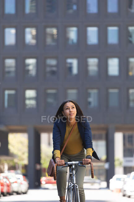 Mujer afroamericana montando bicicleta en la calle. estilo de vida durante la pandemia de coronavirus covid 19. - foto de stock
