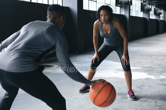 Африканские американец и женщина стоят в пустом городском здании и играют в баскетбол. здоровый образ жизни. — стоковое фото