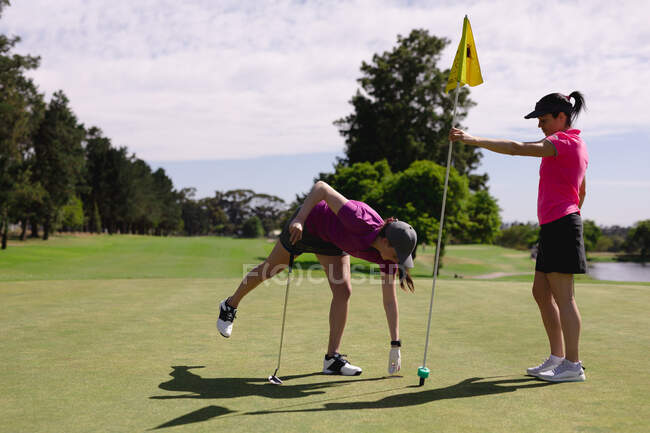 Duas mulheres caucasianas a jogar golfe, uma segurando a bandeira, uma a tirar a bola do buraco. esporte lazer hobbies golfe saudável ao ar livre estilo de vida. — Fotografia de Stock