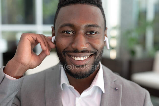 Retrato de un hombre de negocios afroamericano parado en un café mirando la cámara. escuchar música con auriculares. hombre de negocios en la salida en la ciudad. - foto de stock