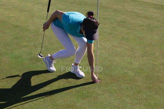 Mujer caucásica jugando golf tomando pelota desde el agujero en el campo de golf. deporte ocio aficiones golf estilo de vida al aire libre saludable. - foto de stock