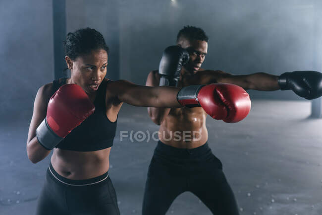 Африканський американець і жінка у боксерських рукавицях кидають удари в повітря в порожньому будинку. Здоровий спосіб життя в місті. — стокове фото