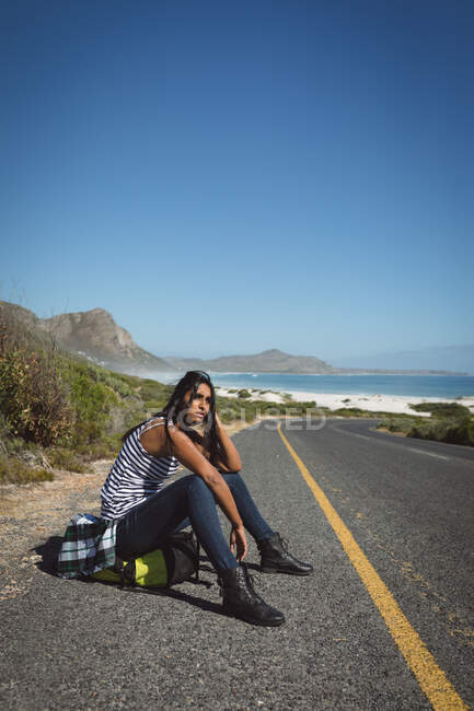 Mischlingshündin sitzt am Straßenrand und trampt. Sommerreisen auf einer Landstraße an der Küste. — Stockfoto