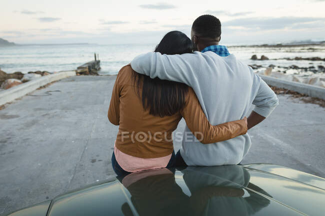Diverse couple sitting on a convertible car and embracing. Summer road trip on a country highway by the coast. — Stock Photo