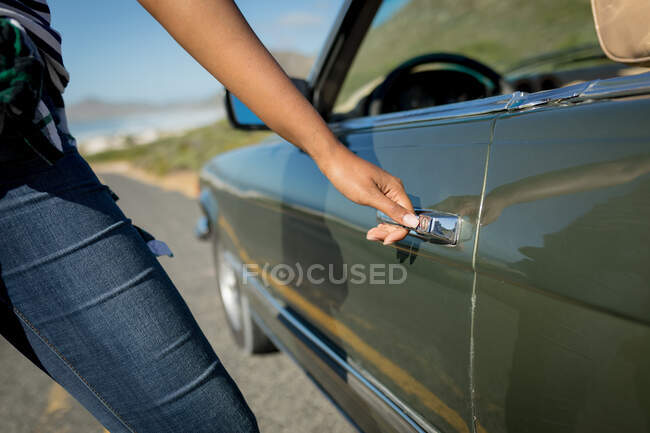 Woman on sunny day entering the convertible car. summer road trip on a country highway by the coast. — Stock Photo