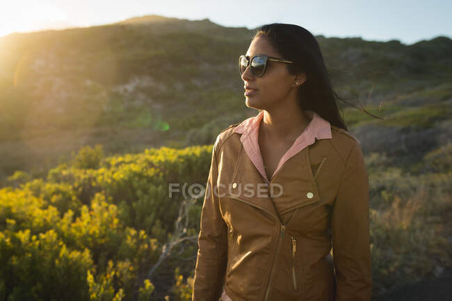 Mujer de raza mixta de senderismo en las montañas por la costa. verano viaja en una carretera rural por la costa. - foto de stock