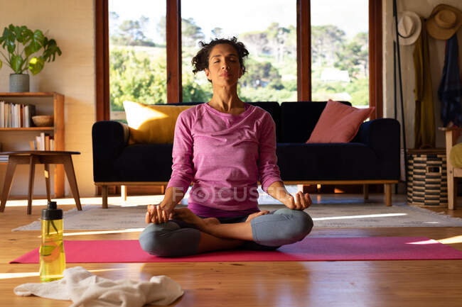 Mujer caucásica con los ojos cerrados meditando, practicando yoga en casa. Permanecer en casa en aislamiento durante el bloqueo de cuarentena. - foto de stock
