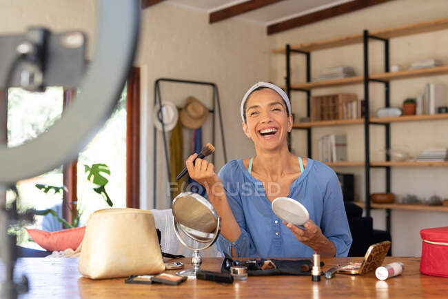 Усміхнена біла жінка, відеоблог, нанесення макіяжу, використовуючи пензлик для макіяжу вдома. Перебування вдома в самоізоляції під час карантину . — стокове фото
