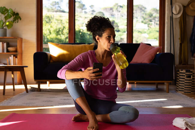 Mujer caucásica bebiendo agua tomando un descanso de hacer ejercicio en casa. Permanecer en casa en aislamiento durante el bloqueo de cuarentena. - foto de stock