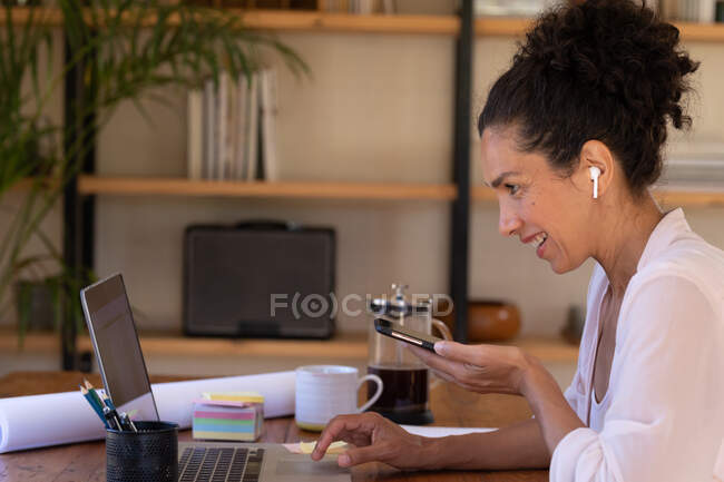 Caucasian woman using smartphone and laptop on video call, working from home. Staying at home in self isolation during quarantine lockdown. — Stock Photo
