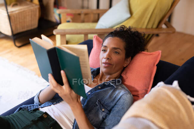 Kaukasische Frau liest Buch, das zu Hause auf dem Sofa liegt. Zu Hause bleiben in Selbstisolierung während Quarantäne Lockdown. — Stockfoto