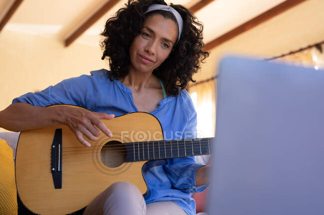 Caucasian woman playing guitar using laptop sitting on sofa at home. staying at home in self isolation during quarantine lockdown. — Stock Photo