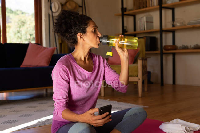 Caucasian woman drinking water taking break from exercising at home. Staying at home in self isolation during quarantine lockdown. — Stock Photo