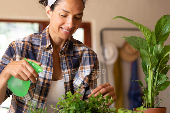 Sonriente mujer caucásica regando plantas en casa. Permanecer en casa en aislamiento durante el bloqueo de cuarentena. - foto de stock