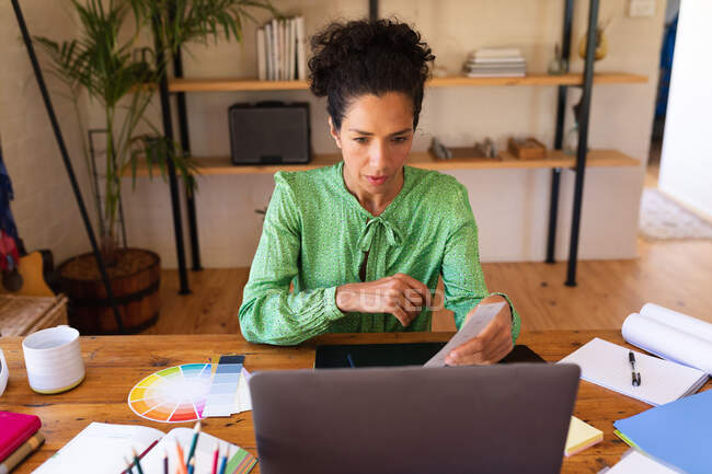 Caucasian woman using laptop working from home, holding colour swatch. staying at home in self isolation during quarantine lockdown. — Stock Photo