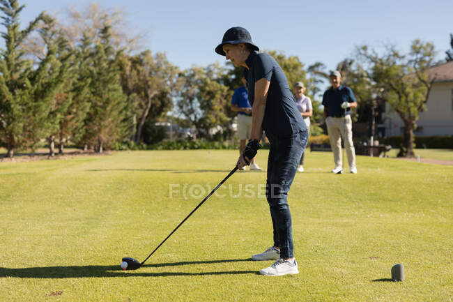 Three caucasian senior men and women watching woman preparing for a shot on the green. Golf sports hobby, healthy retirement lifestyle — Stock Photo