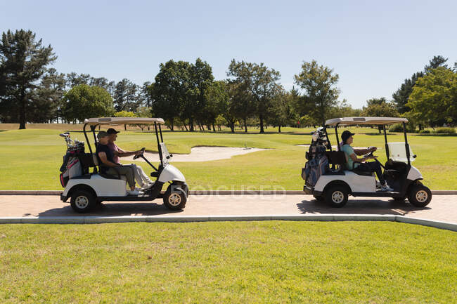 Two caucasian senior couples driving golf buggy on golf course talking and smiling. golf sports hobby, healthy retirement lifestyle. — Stock Photo