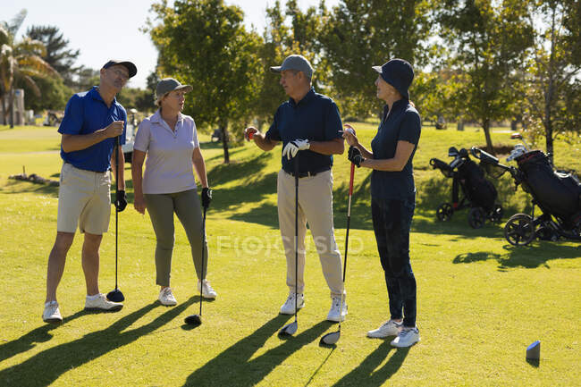 Чотири кавказькі старші чоловіки і жінки тримають гольф-клуби і розмовляють. Гольф спортивне хобі, здоровий спосіб життя на пенсії — стокове фото
