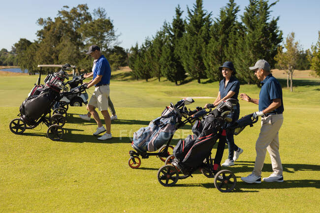 Quattro uomini e donne caucasici anziani che attraversano il campo da golf con sacchi da golf. Golf sport hobby, sano stile di vita pensionamento — Foto stock