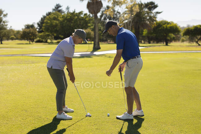 Hombre y mujer mayores caucásicos preparándose para disparar en el green. deportes de golf hobby, estilo de vida de jubilación saludable. - foto de stock