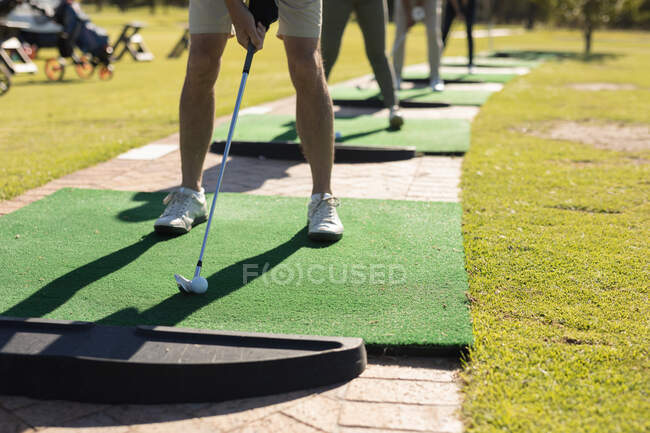 Drei kaukasische Senioren und eine Frau mit Golfschläger bereiten sich auf den Schlag auf dem Grün vor. Golf-Sport-Hobby, gesunder Lebensstil im Ruhestand. — Stockfoto
