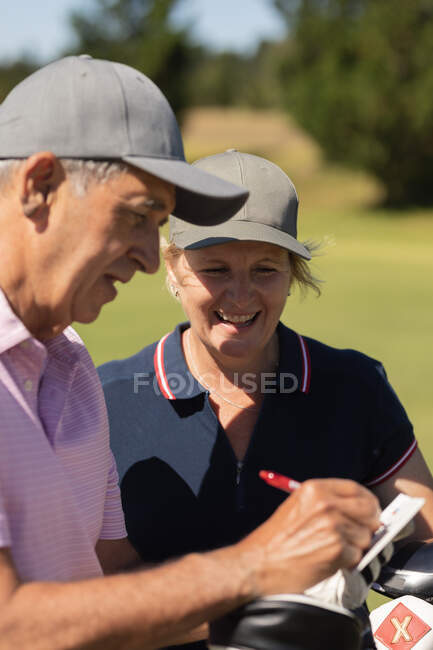 Hombre y mujer mayores caucásicos escribiendo puntos en un cuaderno. Golf deportes hobby, estilo de vida de jubilación saludable. - foto de stock