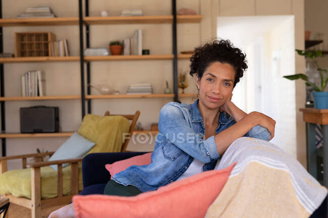 Портрет білої жінки, що сидить на дивані і посміхається до камери, розслабляється вдома. Перебування вдома в самоізоляції під час карантину . — стокове фото