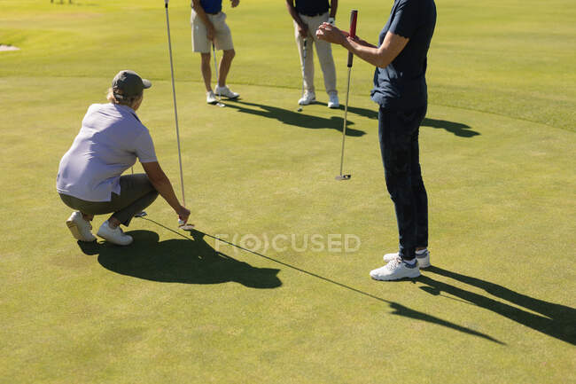 Drei kaukasische ältere Männer und Frauen beobachten, wie Frauen den Ball auf dem Grün vorbereiten. Golf-Sport-Hobby, gesunder Lebensstil im Ruhestand — Stockfoto