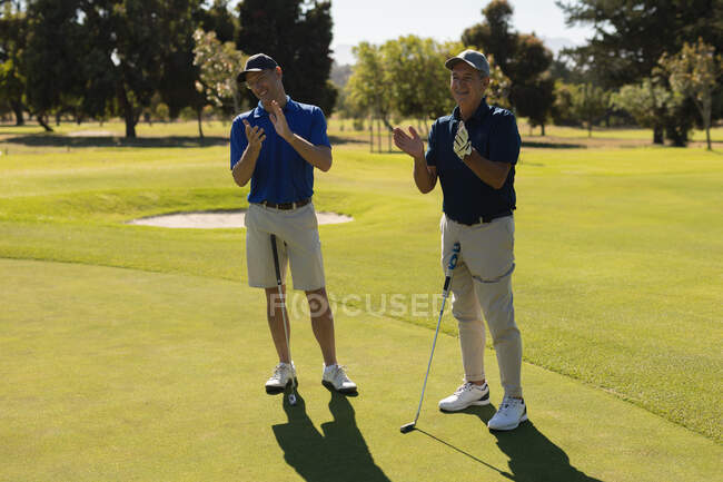 Two caucasian senior men holding golf clubs and clapping. golf sports hobby, healthy retirement lifestyle — Stock Photo