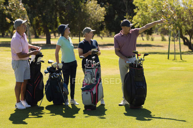 Cuatro hombres y mujeres mayores caucásicos sosteniendo bolsas de golf y hablando. deportes de golf hobby, estilo de vida de jubilación saludable - foto de stock