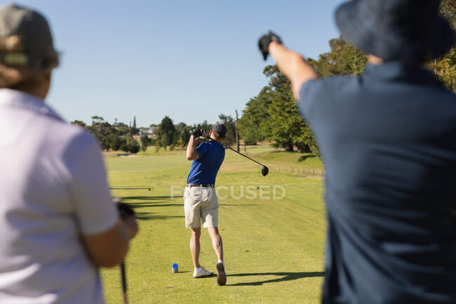Caucasian senior man holding golf club preparing for shot on the green with friends watching. Golf sports hobby, healthy retirement lifestyle. — Stock Photo