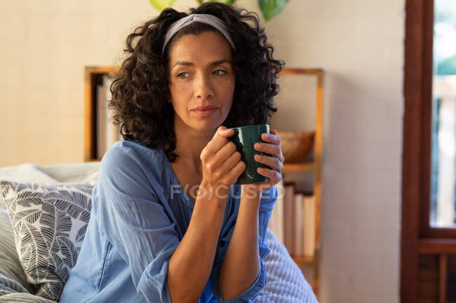 Mulher caucasiana cuidadosa segurando caneca verde sentado no sofá em casa. Ficar em casa em auto-isolamento durante o bloqueio de quarentena. — Fotografia de Stock