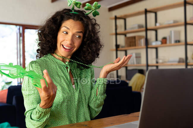 Kaukasische Frau in grün gekleidet mit Shamrock Deely Boppers für st patrick 's day talking while video call. Während der Quarantäne zu Hause bleiben und sich selbst isolieren. — Stockfoto