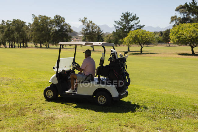 Старший белый мужчина за рулем гольф-багги на поле для гольфа улыбается. Спортивное увлечение гольфом, здоровый пенсионный образ жизни. — стоковое фото