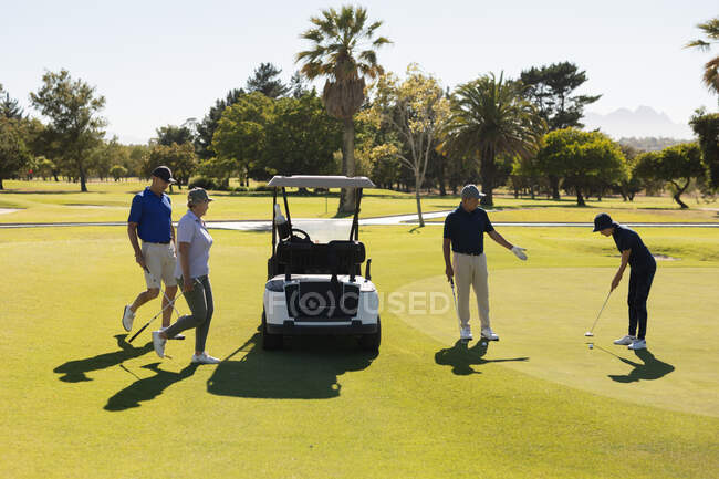 Four caucasian senior men and women preparing to take the shot on the green. golf sports hobby, healthy retirement lifestyle — Stock Photo