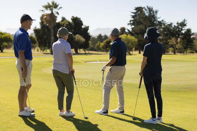 Чотири кавказькі старші чоловіки і жінки готуються взяти постріл на зелений. гольф спортивне хобі, здоровий спосіб життя на пенсії — стокове фото