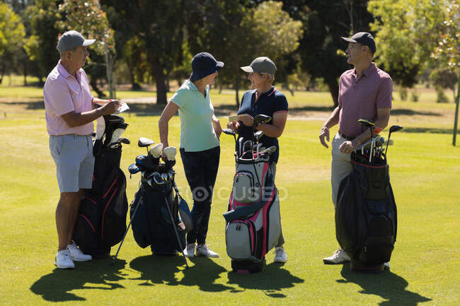 Чотири кавказькі старші чоловіки і жінки тримають сумки для гольфу і розмовляють. гольф спортивне хобі, здоровий спосіб життя на пенсії — стокове фото