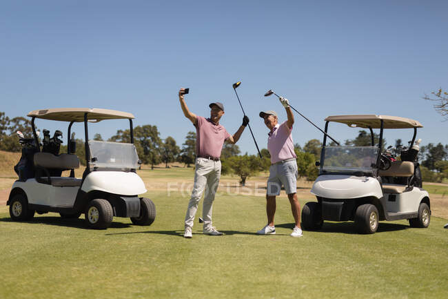 Deux hommes âgés caucasiens tenant des clubs de golf et prenant un selfie. Golf passe-temps sportif, mode de vie sain à la retraite — Photo de stock