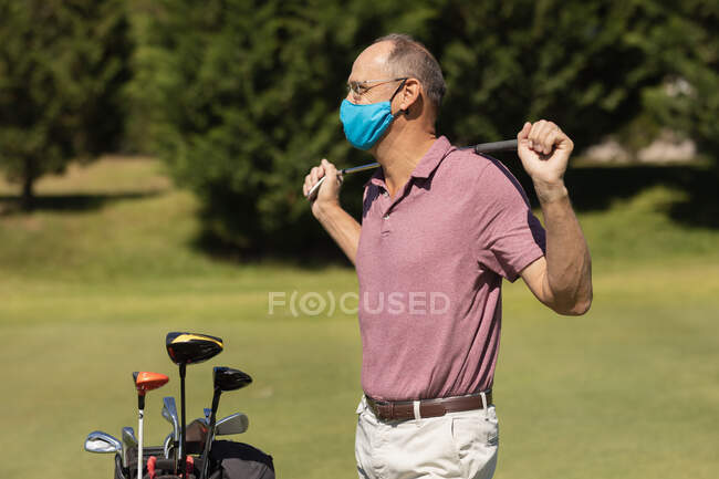 Homme âgé caucasien portant un masque facial tenant club de golf. Golf passe-temps sportif, mode de vie sain à la retraite pendant le coronavirus covid 19 pandémie. — Photo de stock