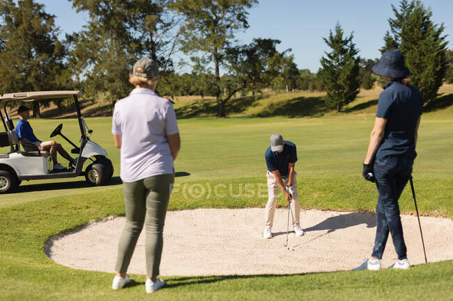 Due donne anziane caucasiche che guardano l'uomo che si prepara a sparare al bunker. sport di golf hobby, sano stile di vita pensione. — Foto stock