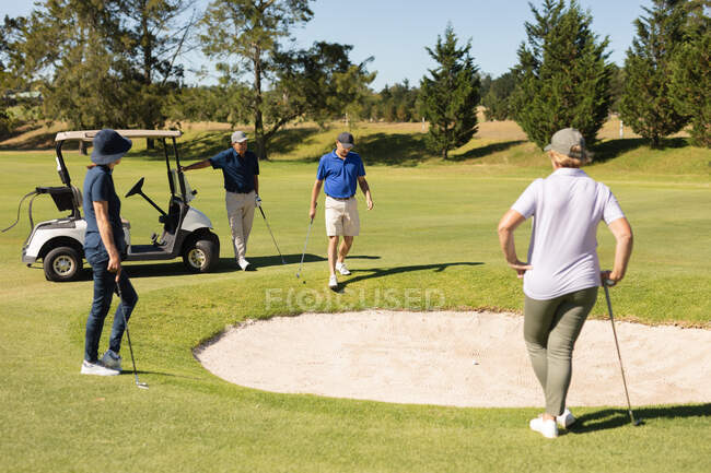 Quatre hommes et femmes âgés caucasiens rassemblés autour du bunker. Golf passe-temps sportif, mode de vie sain à la retraite. — Photo de stock