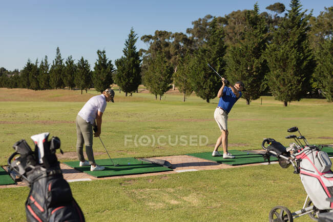 Caucásico hombre y mujer senior sosteniendo club de golf preparándose para el tiro en el green. Golf deportes hobby, estilo de vida de jubilación saludable. - foto de stock