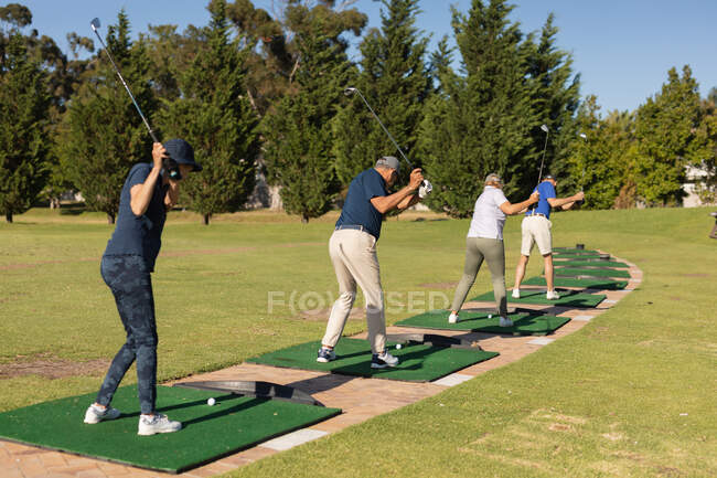 Hombres mayores caucásicos y una mujer sosteniendo club de golf preparándose para el tiro en el green. deportes de golf hobby, estilo de vida de jubilación saludable. - foto de stock