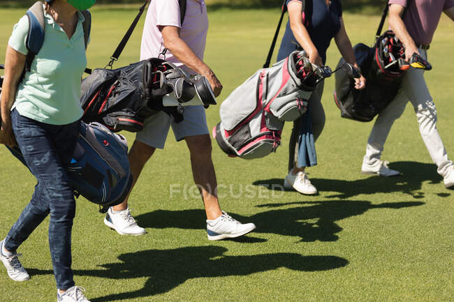 Четверо старших мужчин и женщин ходят по полю для гольфа с сумками для гольфа. Спортивное увлечение гольфом, здоровый пенсионный образ жизни во время коронавирусной ковиды 19 пандемии. — стоковое фото