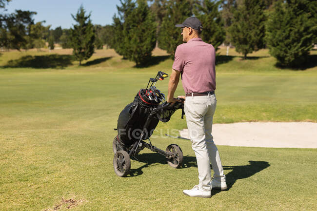Homem idoso caucasiano a atravessar o campo de golfe com saco de golfe. Esportes de golfe passatempo, estilo de vida de aposentadoria saudável — Fotografia de Stock